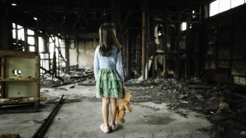 Six year old girl with teddy bear standing in fire damaged building