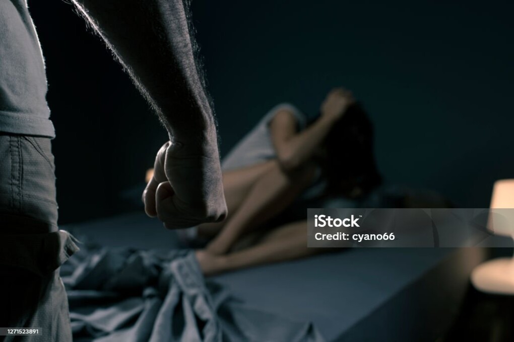 Man threatening a woman in the bedroom, she is scared and lying in bed, domestic violence concept