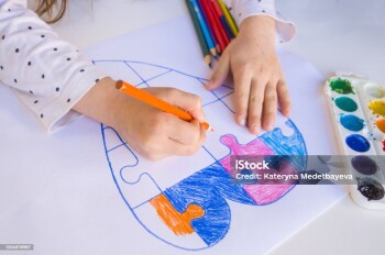 A child is drawing colorful heart with jigsaw puzzle on white background as a symbol of autism, with colorful pencils and watercolors.