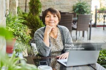 Portrait of adult businesswoman with laptop at table in summer cafe, working outside and smiling at the camera. Self-employed freelancer elderly woman concept