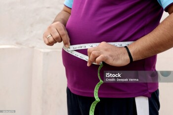 A asian men measures his fat belly with a measuring tape on a plain background