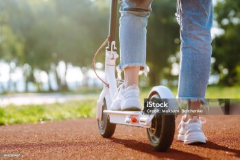 Woman riding electric kick scooter outdoors at sunset, closeup. Ecological transportation concept.