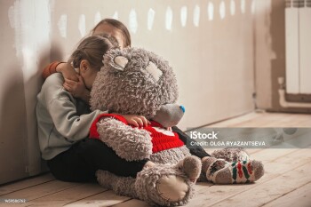 two sisters of different ages hugged and crying in the attic of the house, their big toy bear is with them, they are scared