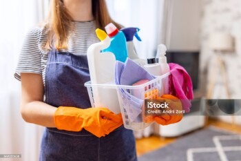Woman in rubber gloves with basket of cleaning supplies ready to clean up her apartment. Housewife has many household chores, domestic work and professional cleaning service. Low depth of field