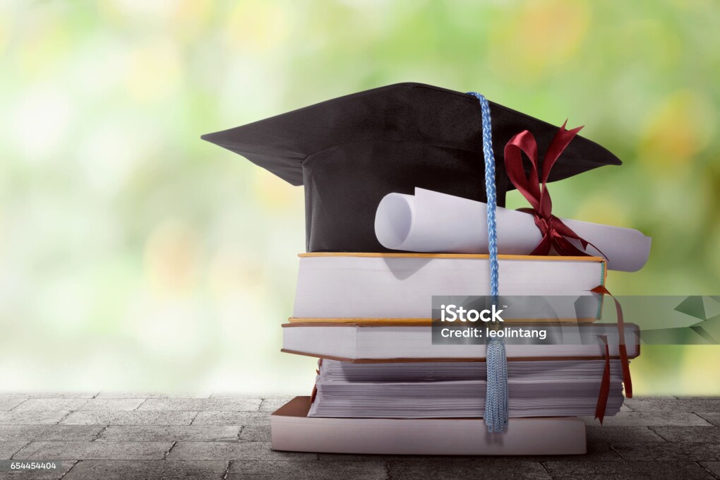 Graduation hat with degree paper on a stack of book against blurred background