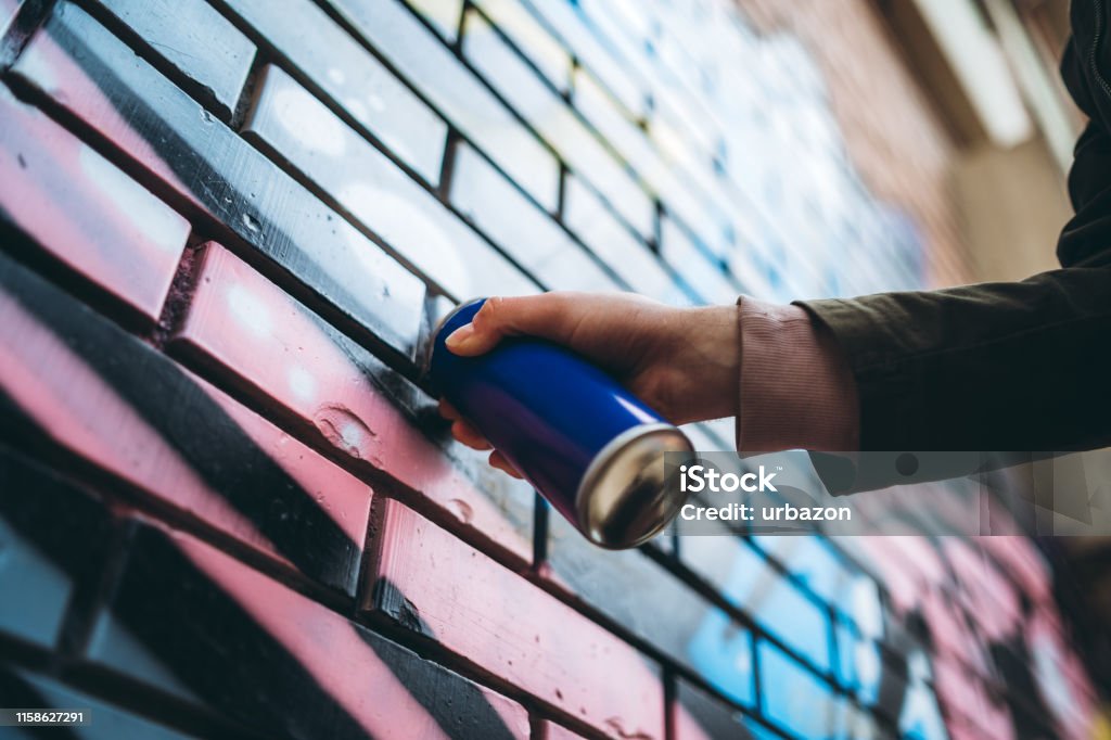 Young caucasian graffiti artist with dreadlocks painting graffiti.