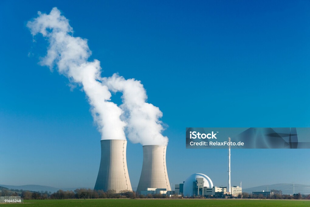 Nuclear power station with two steaming cooling towers in blue sky.