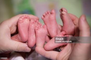 A mother is holding in the hands feet of newborn triplets baby.