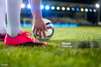 Soccer player putting sports ball on field grass close up