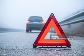 Shot of a emergency triangle sign next to broken car.