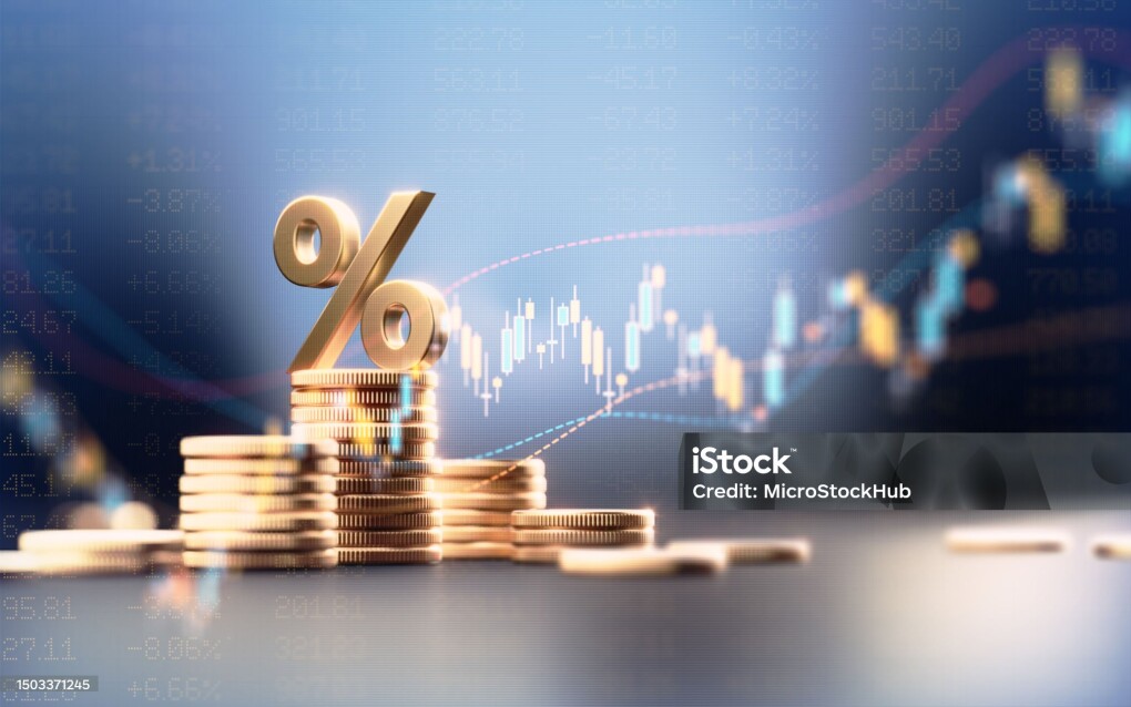 Percentage sign on top of coin stacks before blue financial graph. Horizontal composition with copy space. Business and finance concept.