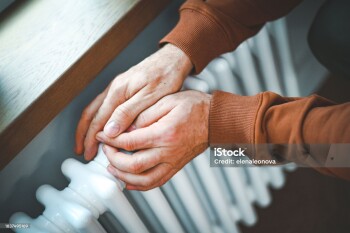 Mature adult man warms himself by the radiator in the room