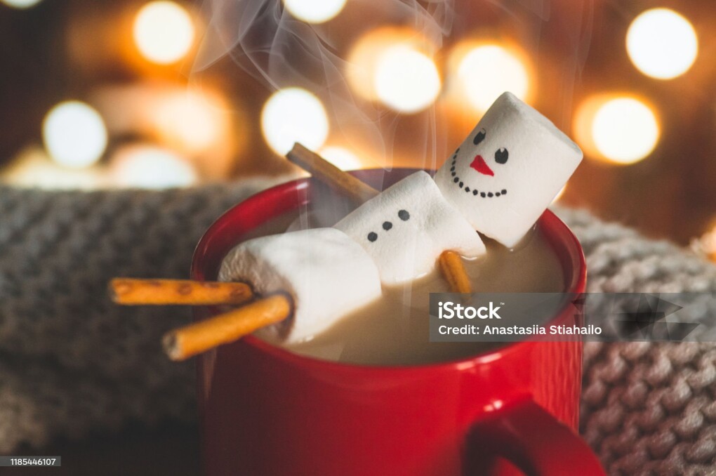 Red mug with hot chocolate with melted marshmallow snowman on bokeh background