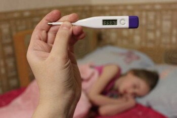 The girl is lying in bed and very sick. The temperature on the thermometer is 39.6.