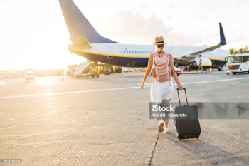 A female tourist walks towards the plane on the runway, dragging personal luggage behind her and carrying a backpack on her back
