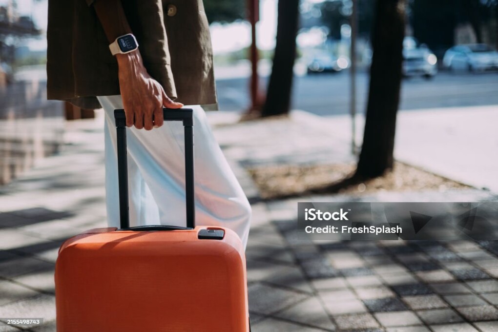 Close-up of a person holding an orange suitcase while walking on a city street during daytime.