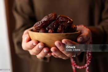 Muslim woman holding dates fruit in a wooden bowl. Traditional Ramadan food.