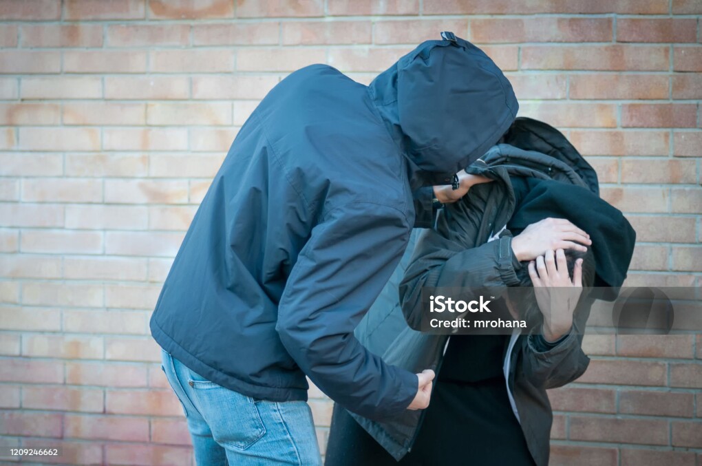 Bullying, aggression and violence scene between two males, one young adult male punches his peer near a bricks wall