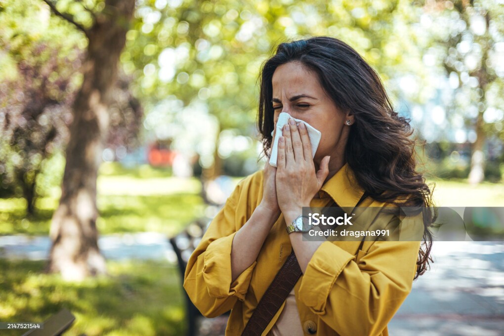 Portrait of unhealthy cute female in yellow top with napkin blowing nose, looks to the source of the allergy, place for advertising. Rhinitis, cold, allergy concept. Pollen allergy symptoms
