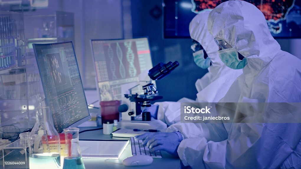 Young multi-ethnic team during coronavirus lab tests. Working on computers. Map of disease outbreaks in background