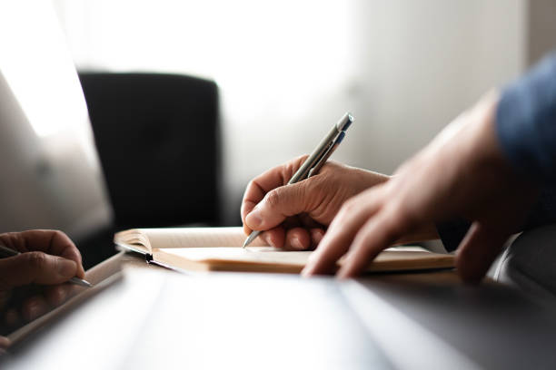 senior man Hands writing in a notebook, focusing on creativity and productivity in a workspace setting