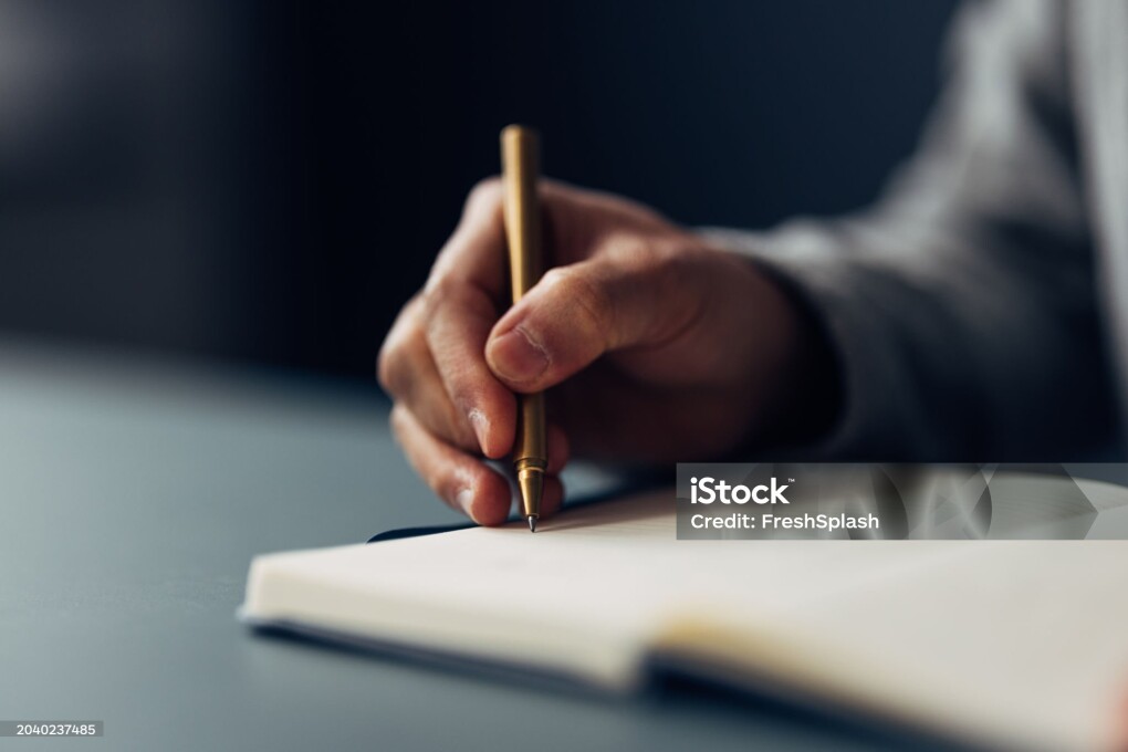 An individual meticulously jotting down notes in a notebook using an elegant pen, with a close-up on the writing hand.