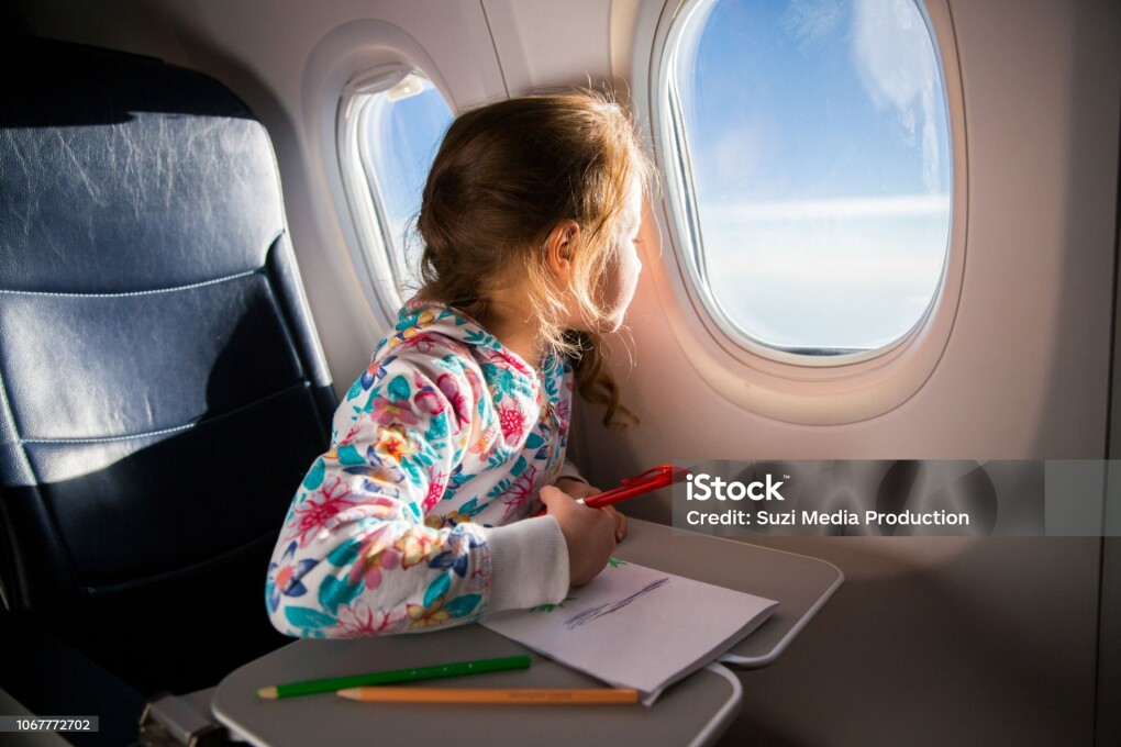 Child drawing picture with crayons in airplane. Little girl occupied while flying in aircraft. Travel with family and kids. Blue sky and sun outside the window