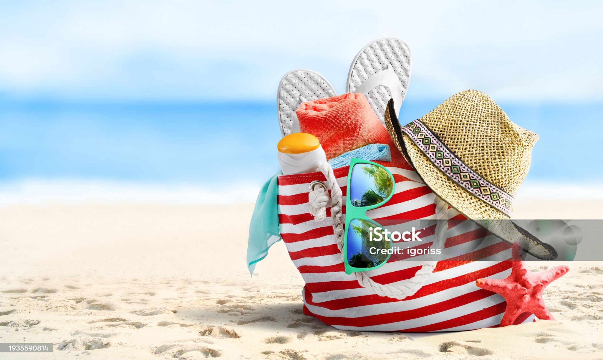Summer vacations concept background. Beach bag, straw hat, flip flops, sunglasses and starfish on sandy beach and azure sea on background.