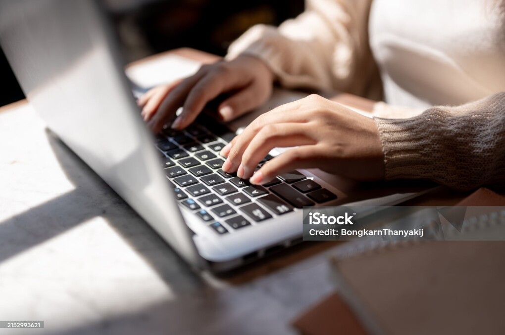 Close-up image of a woman typing on laptop keyboard, working on her laptop computer at a table indoors on a sunny day. businesswoman, student, digital nomad, working remotely