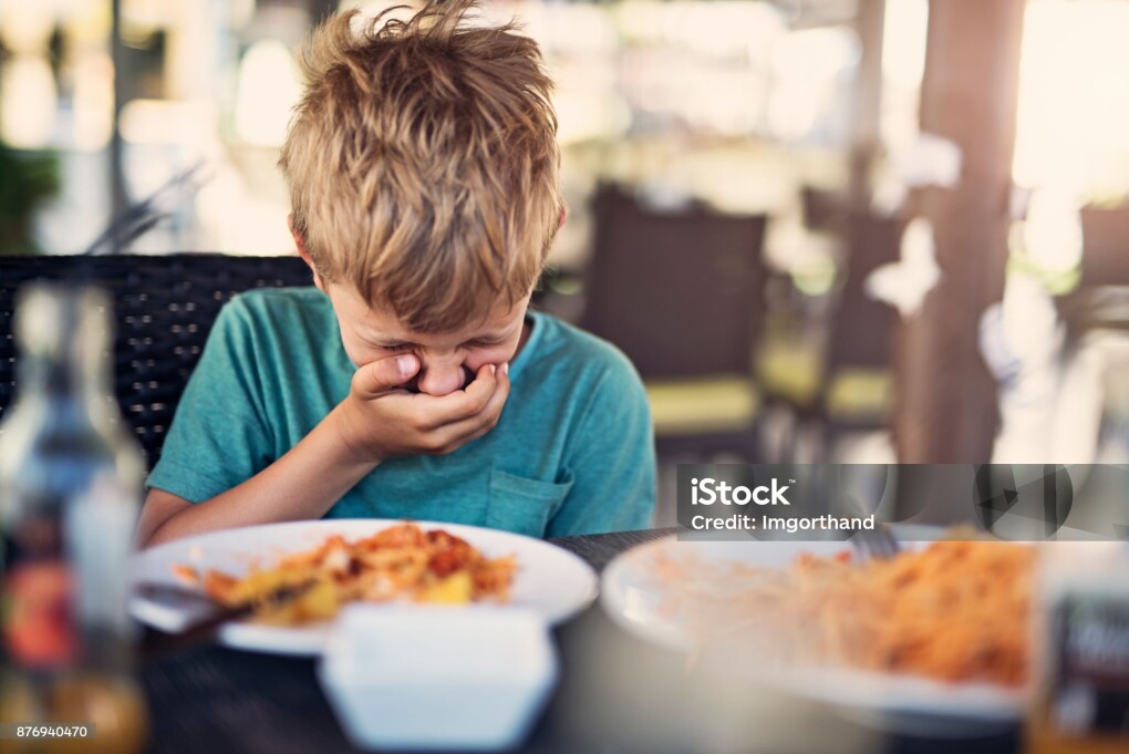 Little boy fussy eater in restaurant. The boy doesnt want to eat and he is even going to throw up even looking at his plate.