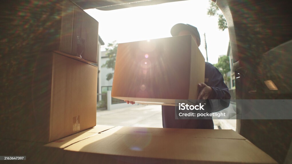 Asian woman delivery courier loading cardboard boxes packages into her car trunk.
