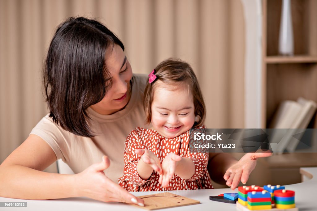 child with down syndrome with educational toys smiles, a cute girl with her mother a teacher