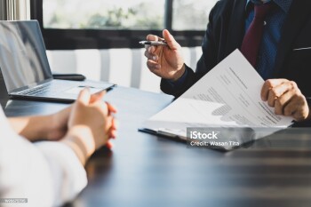 Businessman in suit in his office showing an insurance policy and pointing with a pen where the policyholder must to sign. Insurance agent presentation and consulting insurance detail to customer.