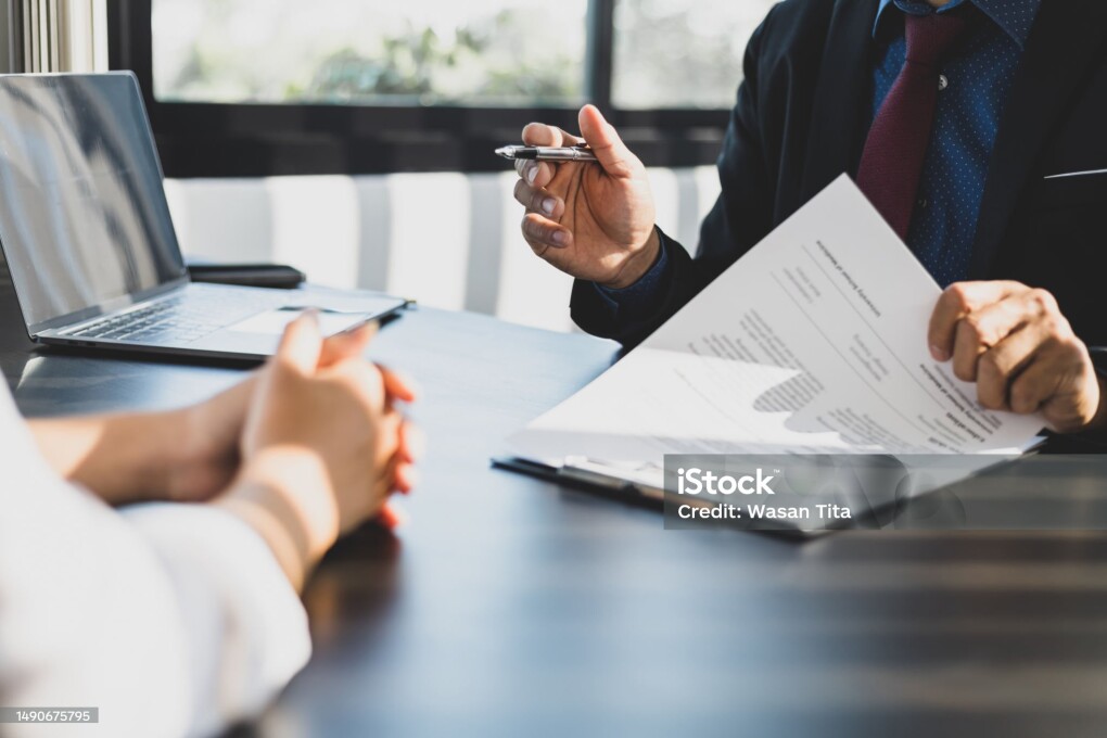 Businessman in suit in his office showing an insurance policy and pointing with a pen where the policyholder must to sign. Insurance agent presentation and consulting insurance detail to customer.