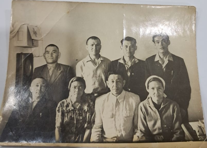 Ұлы Отан соғысының ардагері Жиенбай Суханов жоғарыда сол жақтан бірінші Мұқыр ауылындағы Ә. Жанкелдин атындағы мектеп ұжымындағы әріптестерімен бірге. 1965 жыл.