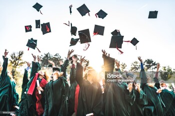 Large group of happy college students celebrating their graduation day outdoors while throwing their caps up in the air.