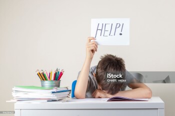 Sad tired frustrated boy sitting at the table with many books and holding help sign. Learning difficulties, education concept.