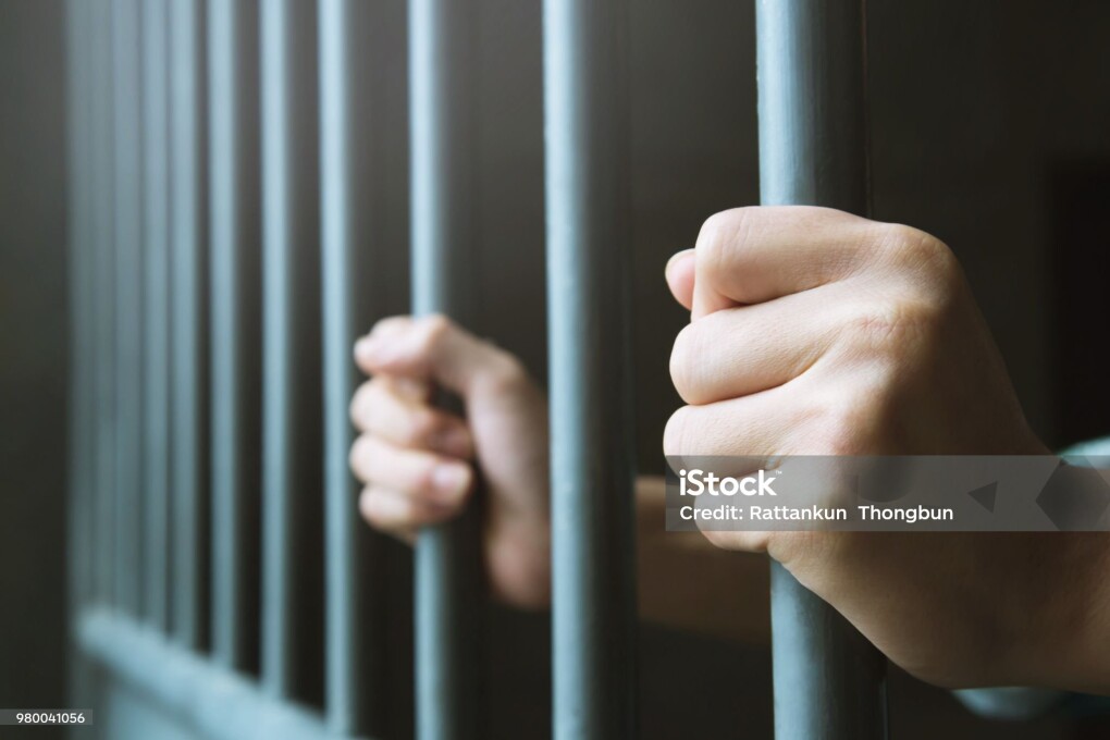 Man in prison hands of behind hold Steel cage jail bars. offender criminal locked in jail.