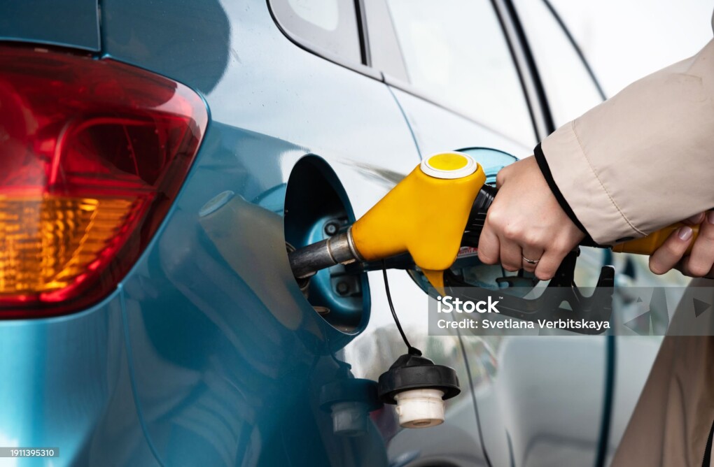 Attractive young woman refueling car at gas station. Female filling diesel at gasoline fuel in car using a fuel nozzle. Petrol concept. Side view
