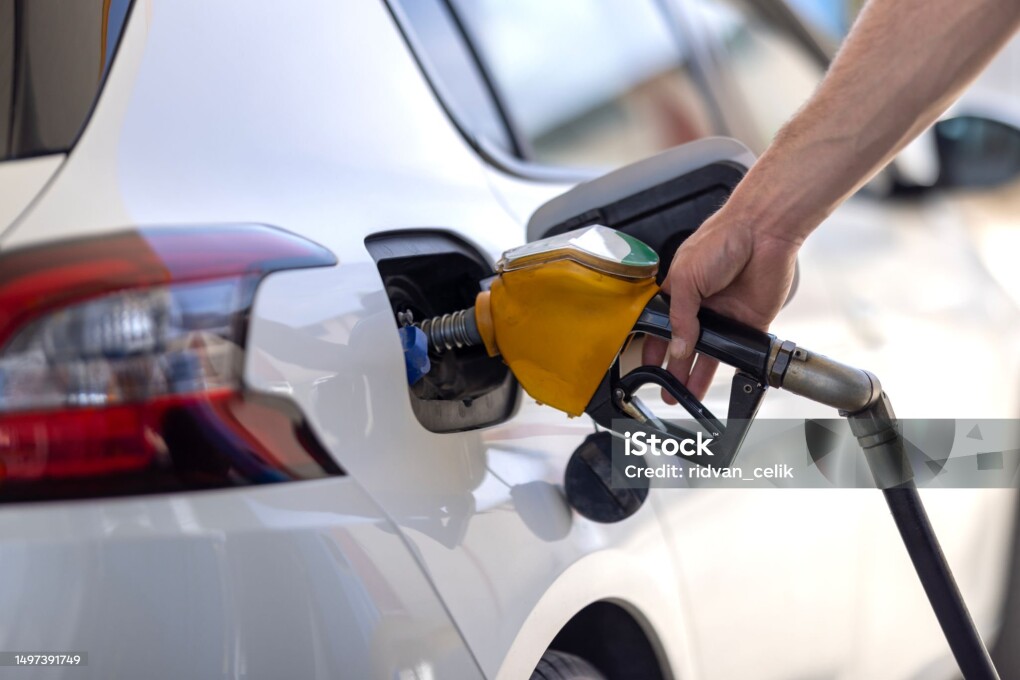 A man holds green fuel nozzle into the gas tank of a car at the gas station
