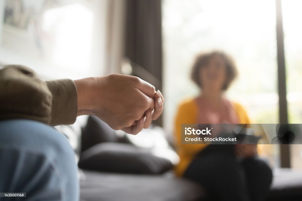 Close-up photo of a teenage girl's hands with fingers crossed nervously. She is in a therapy session with her psychotherapist.