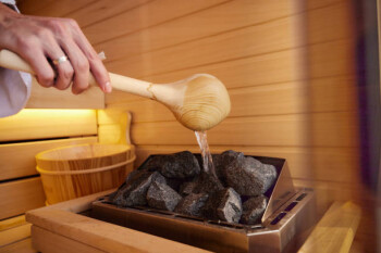 Close up of unrecognizable woman pouring water on hot stones in sauna. Copy space.