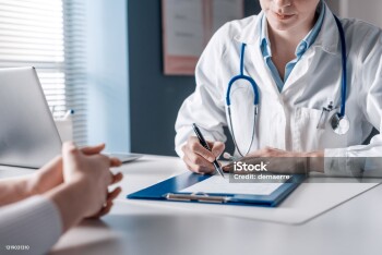 Doctor sitting at desk and writing a prescription for her patient