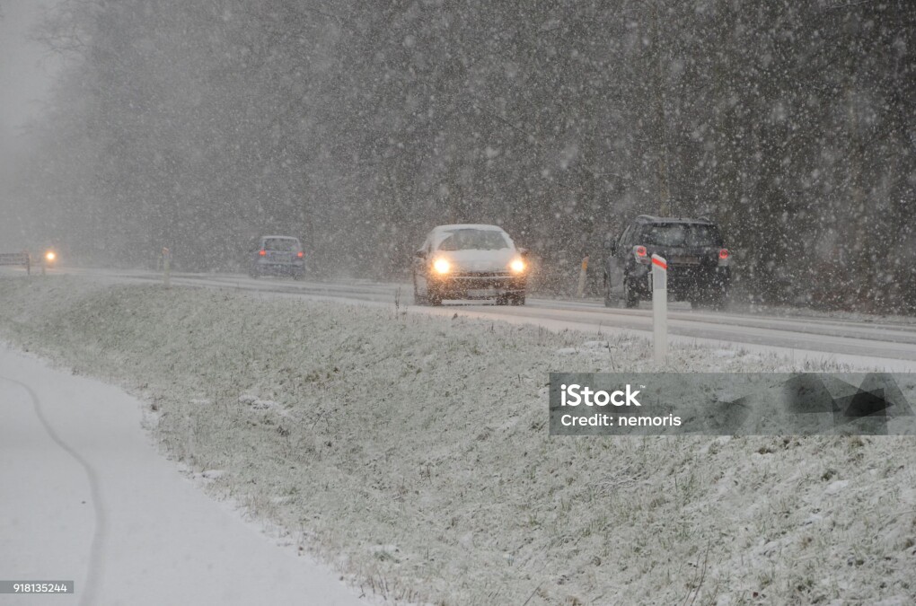 Sparce traffic moving slowly, on a road during heavy snowfall that causes reduced visibility.