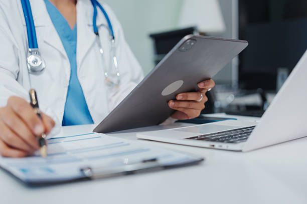 Asian female doctor is reviewing medical records, working on a computer, planning treatment, giving online consultations, and explaining medications to patients via a medical video call in a clinic
