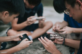 an asian chinese group of teenage boys playing mobile game in the basketball court after school using phone