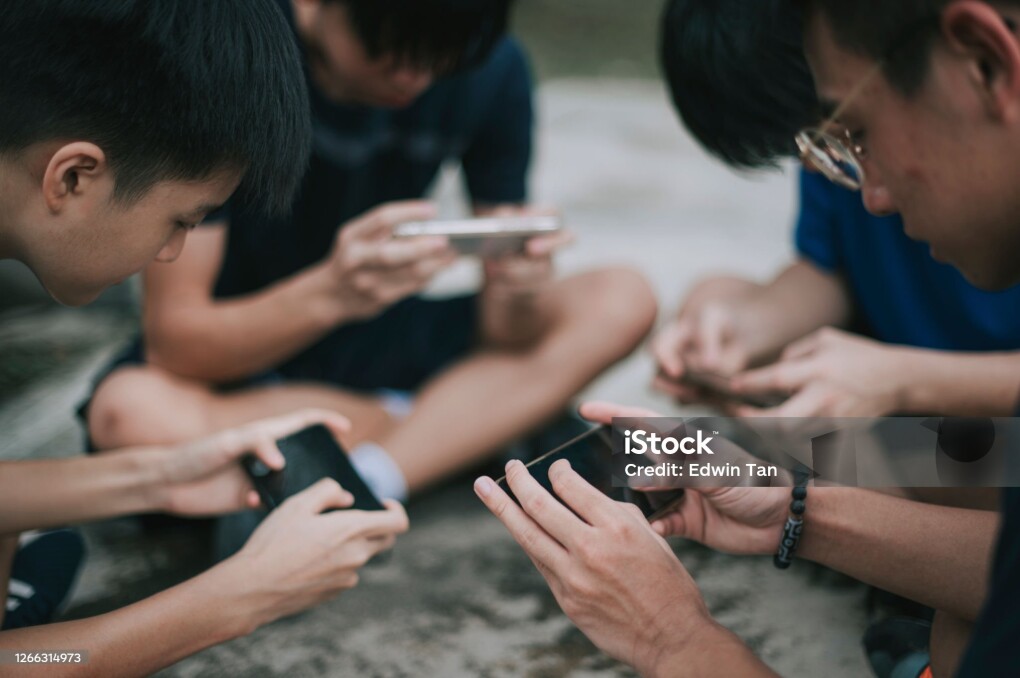 an asian chinese group of teenage boys playing mobile game in the basketball court after school using phone