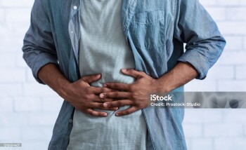Unrecognizable Black Guy Touching Aching Abdomen Having Painful Stomachache Standing Over Gray Studio Background. African Man Suffering From Stomach Inflammation. Gastritis And Abdomen Pain. Cropped