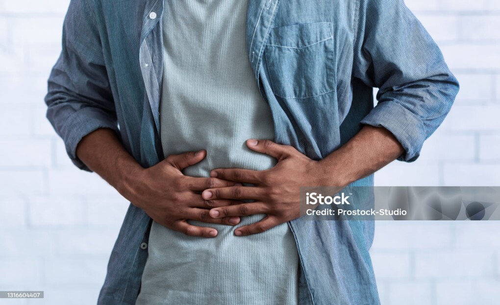 Unrecognizable Black Guy Touching Aching Abdomen Having Painful Stomachache Standing Over Gray Studio Background. African Man Suffering From Stomach Inflammation. Gastritis And Abdomen Pain. Cropped