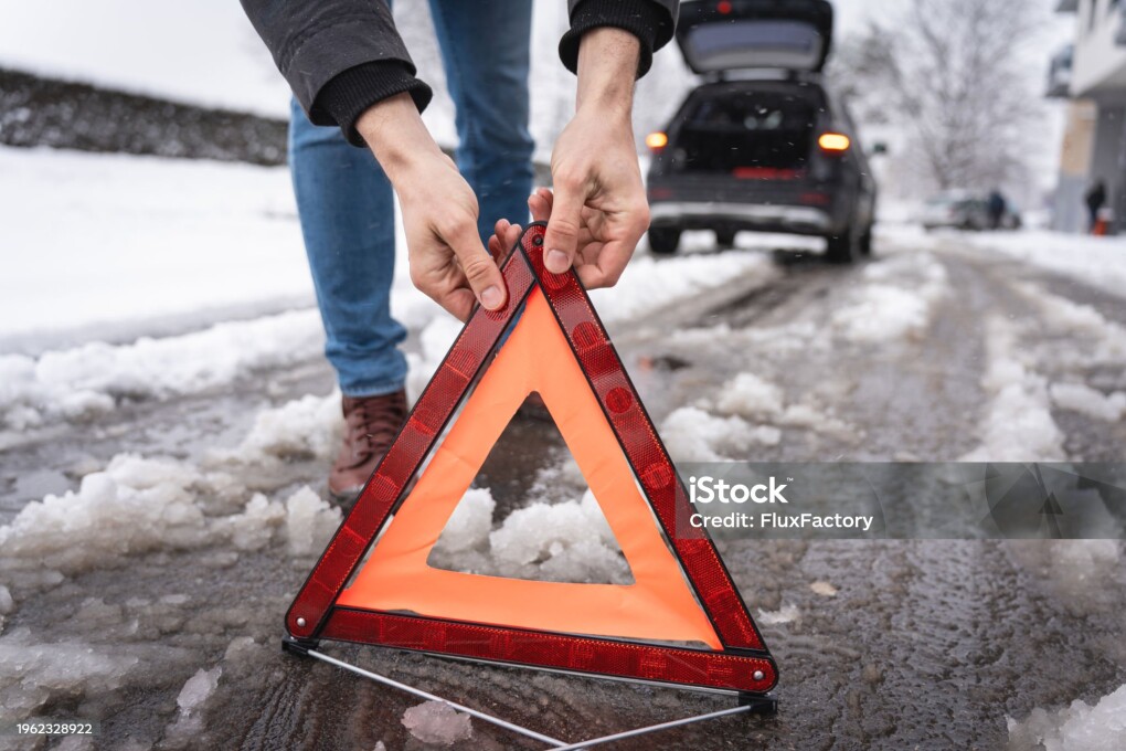 Unrecognizable young Caucasian man, put an warning triangle sign, during an vehicle breakdown on the road, during winter day